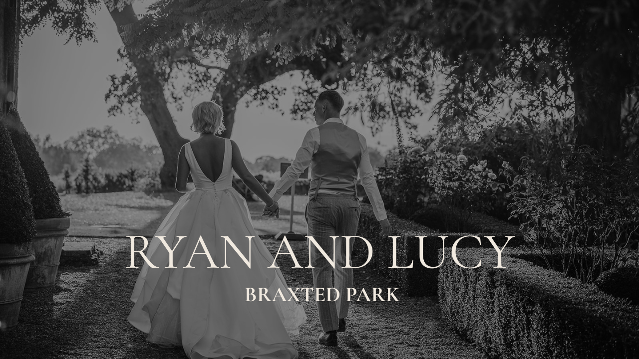 A black and white wedding photo at Braxted Park; the bride and groom are walking away holding hands and looking at each other in the early evening light of the grounds.