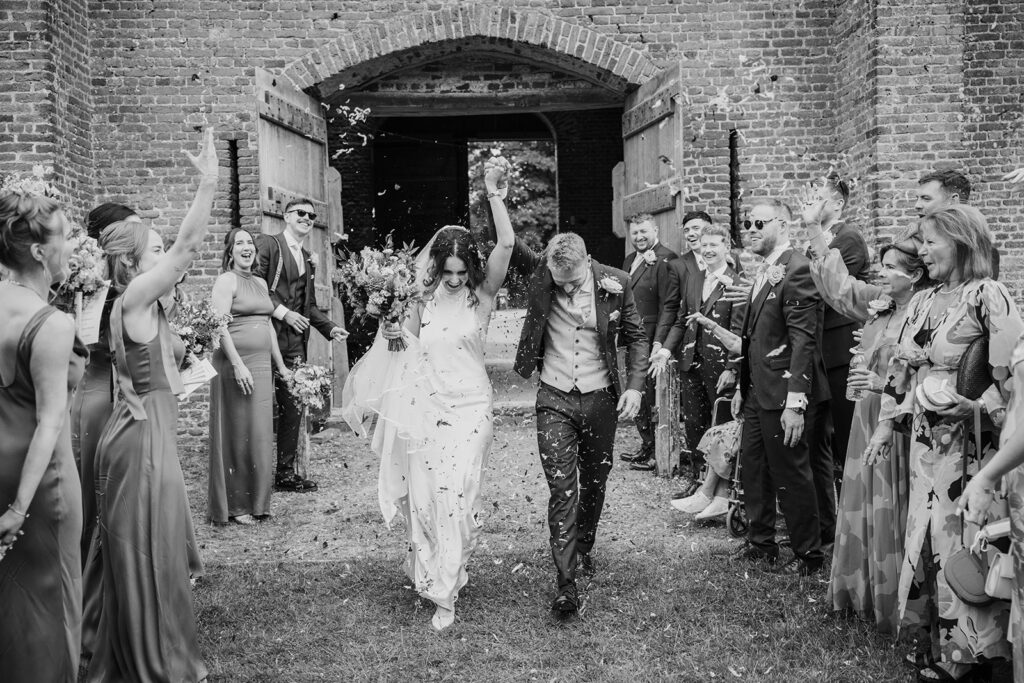A joyful wedding photo of Hannah and Connor walking hand-in-hand through a shower of colorful confetti
